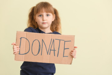 Little girl holding cardboard with text DONATE on color background