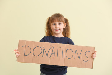 Little girl holding cardboard with text DONATIONS on color background