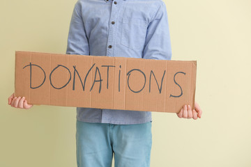 Little boy holding cardboard with text DONATIONS on color background
