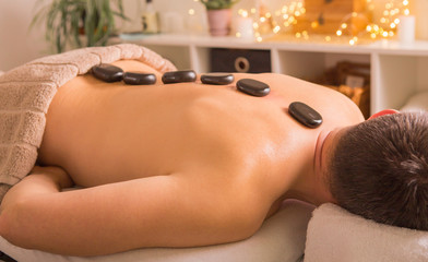 Obraz na płótnie Canvas Man with stones on massage table at spa with body treatment. Person lying and relaxing during 