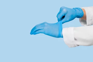 Foto op Plexiglas The doctor puts on sterile gloves on a blue background. Infection control concept. Danger of spread of infection © Nana_studio