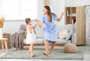 Happy mother and her little daughter dancing at home