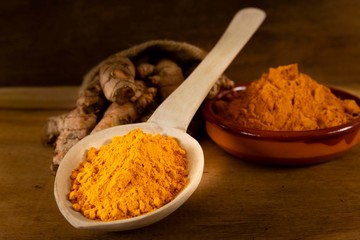 Turmeric powder and roots on a dark wooden surface
