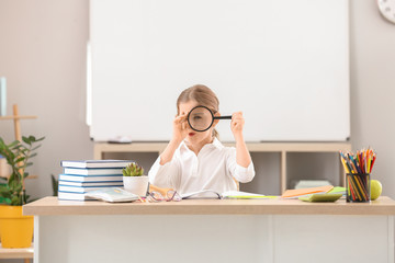 Cute little schoolgirl at desk in classroom