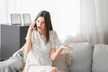 Indignant young woman talking by mobile phone at home