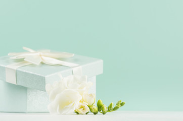 Easter festive background in trendy green mint menthe color on white wood table - fresh white flowers, opened square gift box with knot, closeup.