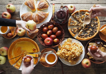 A festive set table with abundant food, pies, eggs, homemade cakes and cutlets.Hands of guests over...