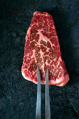 Raw black Angus marbled beef neck steak on a black background with a grill fork