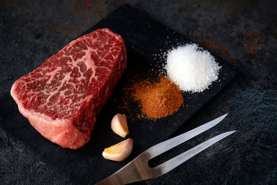 Raw flat iron steak from the neck of beef on a black background with salt and seasonings for the grill