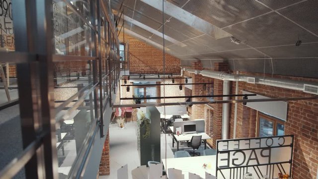 Tilt down high angle shot of modern open space office building with loft interior, brick walls and two floors. There are no people inside