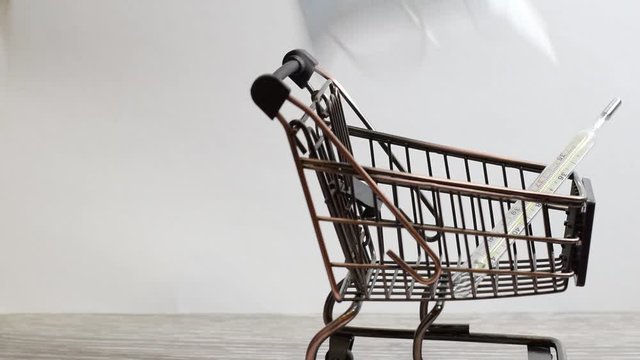 A mini shopping cart with a medical mask and thermometer is wheeled by hand, stopped, and taken out in turn, the mask and thermometer.