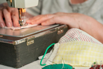 Elderly senior woman working on old sewing machine - making home made face masks against coronavirus spreading, closeup focus detail to finished masks in foreground