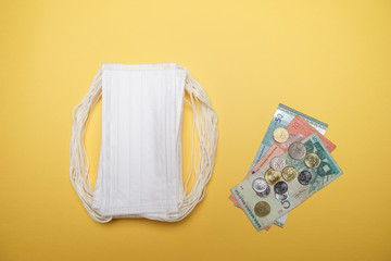 A pile of face mask with Malaysian coin and money isolated over yellow background. Concept during Corona virus outbreak in Malaysia, shortage of face mask increase the demand in higher price.