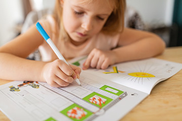 Pretty schoolgirl studying homework during her online lesson at home, social distance during quarantine covid-19, self-isolation, online education concept, home schooler. Workplace in living room.