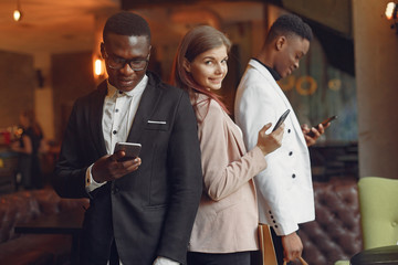 Black men in a cafe. International people. Man in a black suit. Woman in a pink jacket. People with mobile phone.