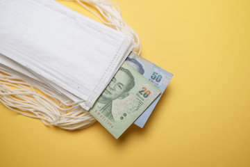 A pile of face mask with Thai Baht money isolated over yellow background. Concept during Corona virus outbreak in Thailand, shortage of face mask increase the demand in higher price.