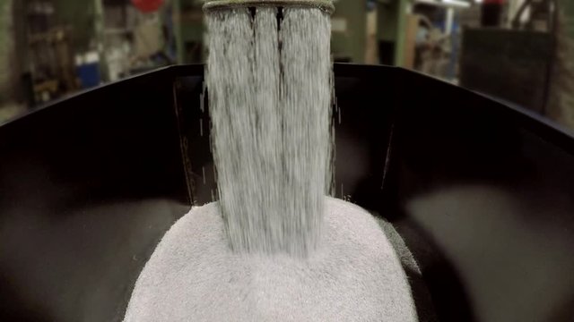 Plastic pellets falling into a metal container. Polymeric industrial extrusion process. Empty to half full.