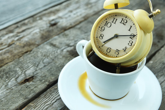 Old retro alarm clock lies in a cup with coffee on a wooden background. Drowned alarm clock in coffee.