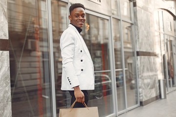 Fototapeta premium Black man in a city. Guy with shopping bags. Man in a white jacket.