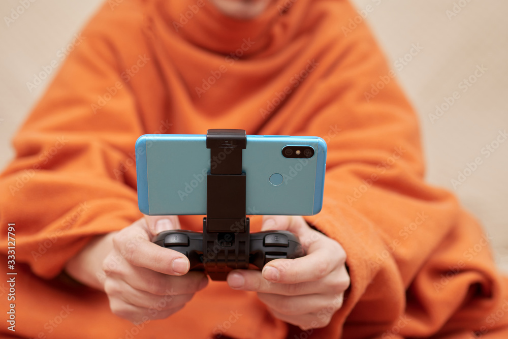 Wall mural boy with an orange blanket, with a gamepad in his hands, and a mobile