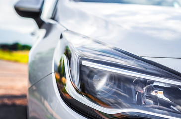 Modern silver car parking on the road. Close up. Headlights detail.
