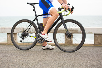 Fototapeta premium Partial view of man riding bicycle. Low section of sportsman in sneakers cycling on bike near body of water. Triathlon concept