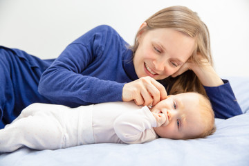 Mother playing with baby girl on bed. Happy young mother looking at adorable little daughter lying on bed. Motherhood concept