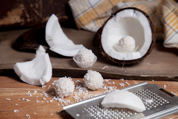 Close up of coconut with white pulp, grater with coconut chip and white candies on wooden background..