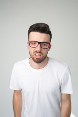 Young man isolated over background. Vertical picture of nerd or weirdo look straight through glasses. Boring and unhappy guy. Stand alon in white shirt.