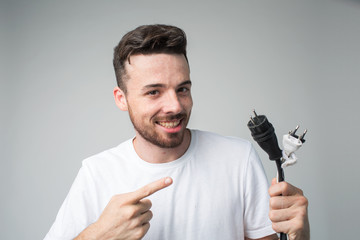 Young man isolated over background. Guy repair master hold cord with socket in hand and point on...