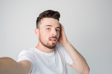 Young man isolated over background. Guy hold camera and take selfie. Posing alone with pleasure. Hold one hand on ear. Mysterious and emotional.