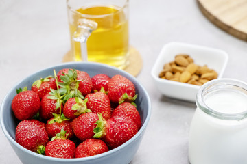 Fresh rustic strawberries lie in a bowl on the table next to fresh milk, almond and warm herbal tea. Morning in the village. Ingredients for a healthy smoothie.