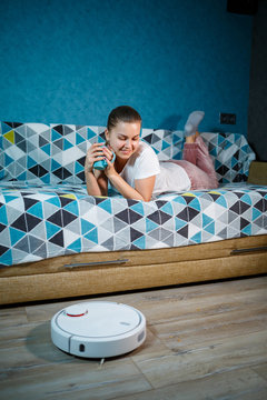 Simple and easy cleaning with modern technology for the household. Girl drinks tea and rests while the vacuum cleaner does the cleaning of the house
