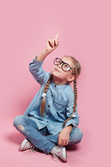 child with glasses points finger up on pink background