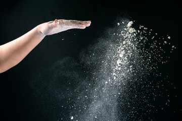 Isolated on black background female hand pours white flour like snow for baking