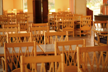 Rows of empty chairs and tables of hte warm sunlit empty cafe / restaurant. Cafe interior background