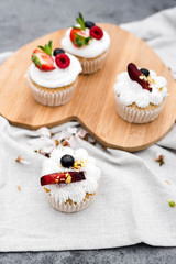 Vegan cupcakes with berries and coconut cream on a wooden board.