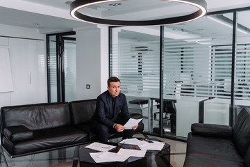 a business man in a suit is sitting on a sofa in a modern office and holding a contract