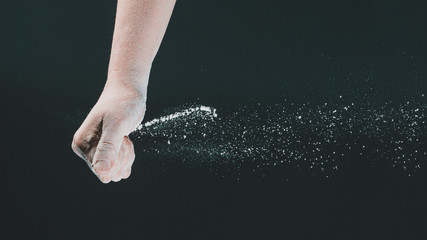 Fototapeta na wymiar On a black background, a woman's hand pours white flour like snow for baking