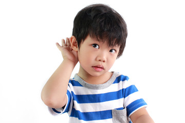 Portrait of little Asian boy with hand by ear against white background.