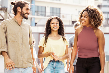 Obraz premium Smiling friends walking outdoors. Cheerful young multiethnic men and women walking and talking together on street. Communication concept