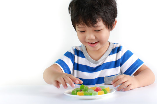 Little Asian boy eating candies on a white background