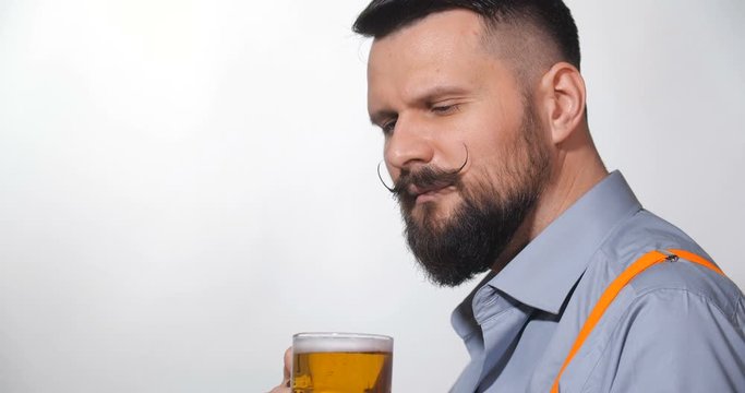 Close up side view  portrait of handsome bearded man with long twisted mustache, toast, drinking beer  from large glass mug  on white background isolated. With free space for writing 4k slow motion.