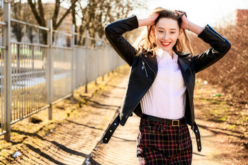 Spring portrait of a smiling beautiful girl with emotions in the sun outdoors in a park. Model is wearing a white blouse and a jacket in front of the camera