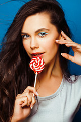 young pretty adorable brunette woman with candy close up posing on blue background, like doll makeup, fashion beauty people concept