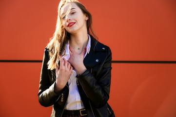 Spring portrait of a smiling beautiful girl with emotions in the sun outdoors on an orange background. Model is wearing a white blouse and a jacket in front of the camera