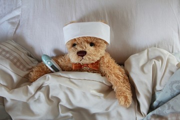 the sick teddy bear in bed with thermometer and head band