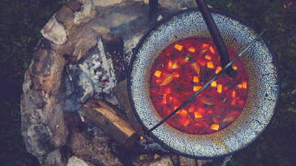 Cooking goulash soup in a cauldron on open fire in the woods