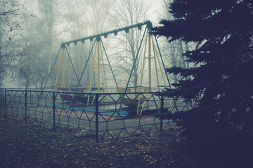 Swing boats in an old abandoned park on a foggy autumn morning