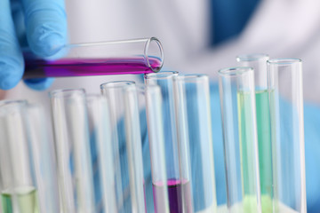 A male chemist holds test tube of glass in his hand overflows a liquid solution of potassium permanganate conducts an analysis reaction takes various versions of reagents using chemical manufacturing